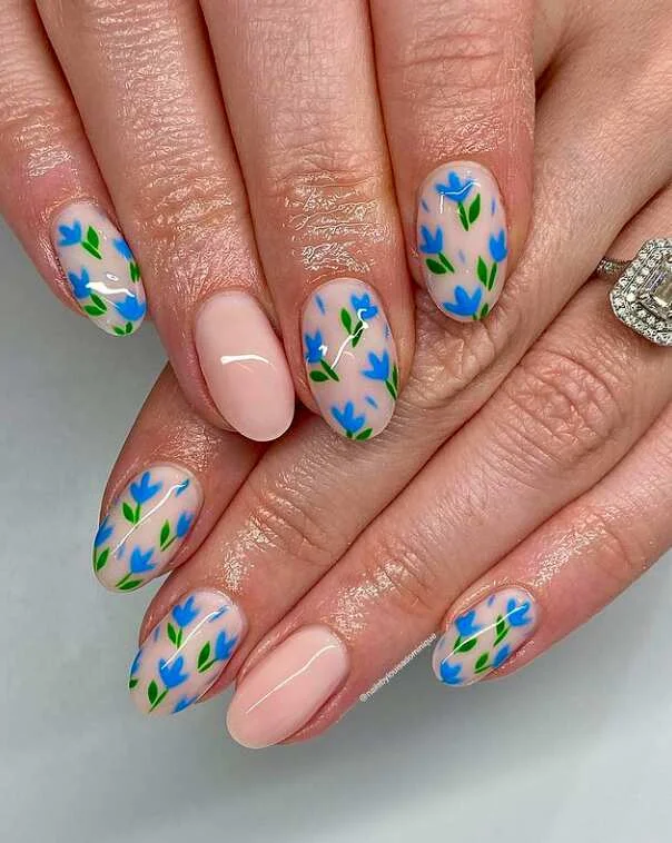 Blue floral nails with delicate round flowers - sophisticated hand showcasing light pink base with soft blue flower petals, featuring white centers and green leaves on round-shaped nails